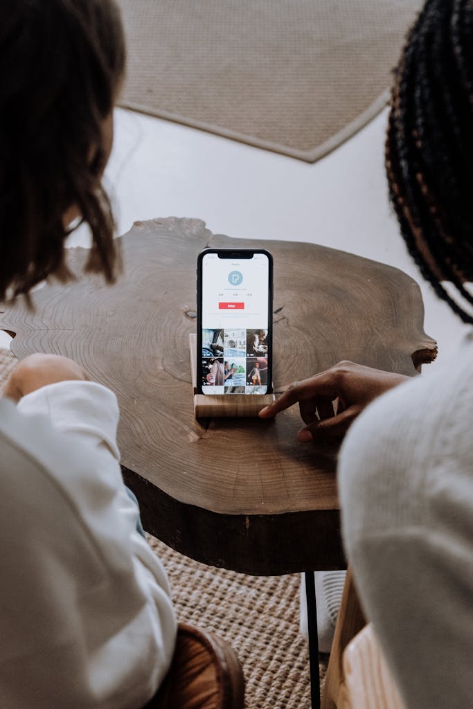 Two individuals engage with a smartphone on a wooden table indoors, highlighting technology in a casual setting.